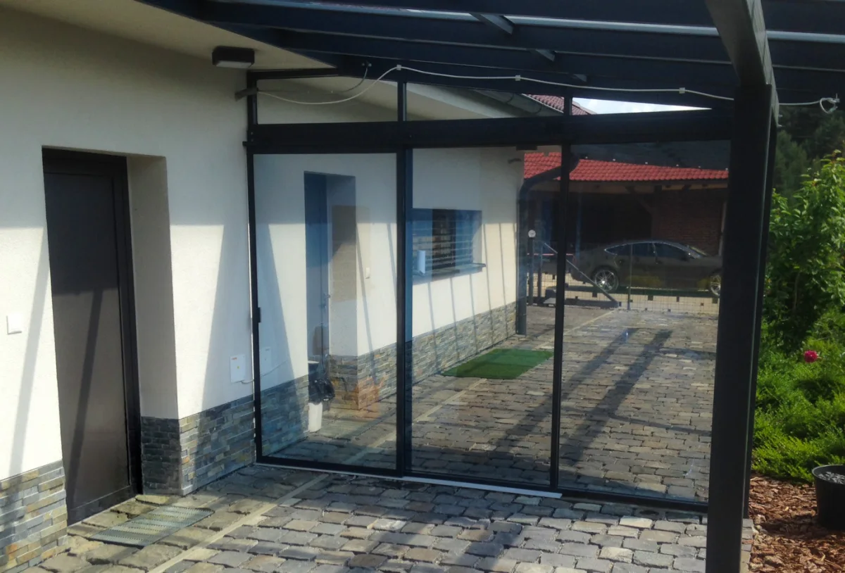 Presklený prístrešok terasy rodinného domu v čiernych hliníkových rámoch s fóliou na skle